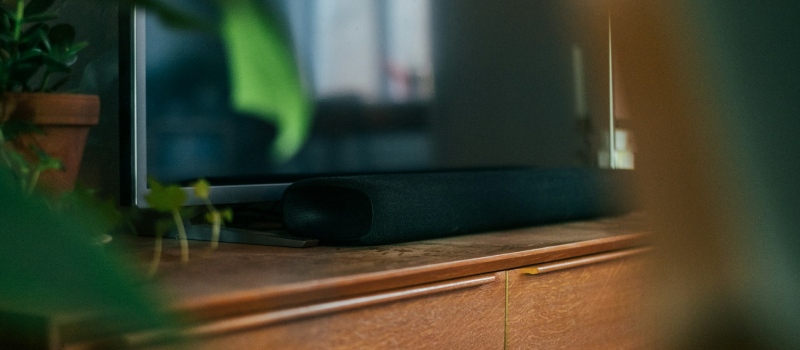 Przenies wieczory filmowe na nowy poziom dzieki soundbarowi Zblizenie na elegancki, ciemny soundbar na drewnianym meblu.